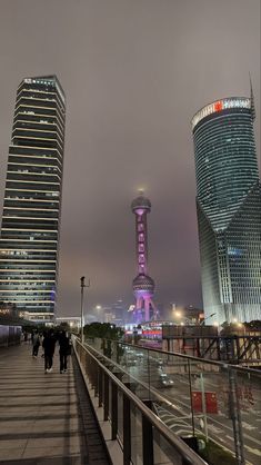 two tall buildings are lit up in the night sky with people walking on either side