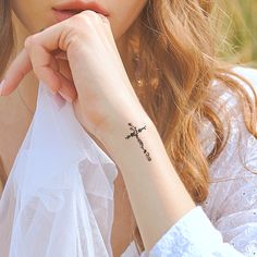 a woman with a small cross tattoo on her left wrist, wearing a white dress