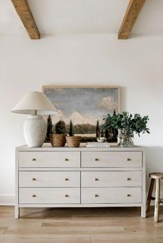 a white dresser with two vases on top and a lamp next to it in a living room