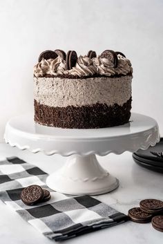 a chocolate cake with oreo cookies on the side sitting on a white cake stand