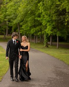 a young man and woman walking down a path in the park holding each other's hands