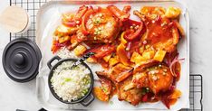 a white plate topped with meat covered in sauce and vegetables next to rice on a cooling rack