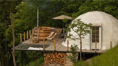 a yurt in the woods with chairs and an umbrella on it's roof