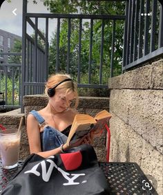 a woman sitting on a bench reading a book and listening to headphones while holding an open book