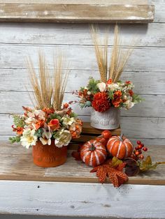 two vases filled with flowers and pumpkins sitting on a wooden shelf next to each other