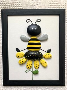 a black frame holding a yellow and black bee on it's back, sitting in front of a white wall