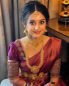 a woman in a red and gold sari sitting on a chair with her hands crossed