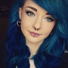 a woman with blue hair and piercings on her nose is posing for the camera