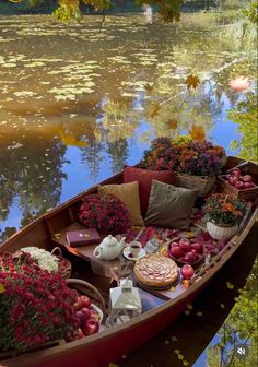 a boat filled with lots of flowers sitting on top of a river next to a forest