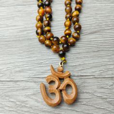 37" Unique Handcrafted Top Quality Tiger Eye Regal Beaded Knotted Necklace with Sandalwood Om Carved Scared Symbol. Sacred Amulet, Protection and Blessing Jewelry Gift. Handcrafted, Comes with A Velvet Pouch. ✥ Mala Necklace: 37" Long - 8mm beads ❀❀❀ Please look closely at photos as part of item description, the product in the images is as the one you will receive and is sold "as is". Please review the description and images prior to purchasing to ensure this item meets your satisfaction. We wel Brown Beaded Necklaces For Meditation And Festivals, Brown 8mm Beads Mala For Festival, Brown Beaded Mala For Festivals, Brown Mala With 8mm Beads For Festival, Brown Wooden Beads For Festivals, Festival Brown Beaded Mala, Bohemian Brown Mala For Festivals, Brown Necklace With 108 Beads For Festivals, Knotted Necklace