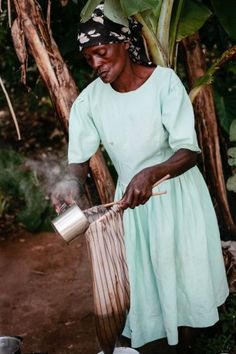 a woman cooking food on top of a stove next to pots and pans in front of trees