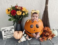 a baby in a pumpkin costume sitting next to some flowers and other halloween decorations on the ground