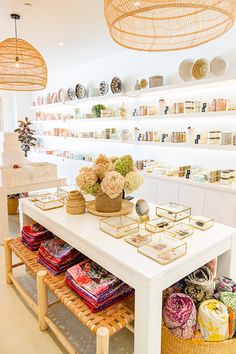 a white table topped with lots of baskets filled with flowers next to shelves full of books