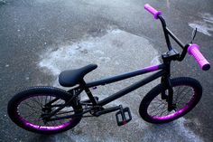 a black and purple bmx bike parked on the side of the road with pink rims