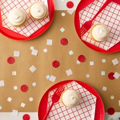 three red plates topped with cupcakes sitting on top of a paper covered table