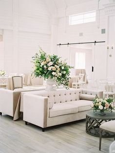 a living room filled with white furniture and flowers on top of it's tables