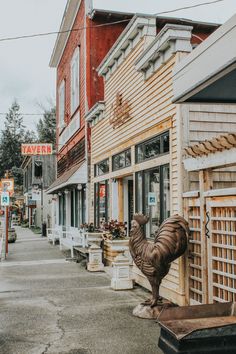 a wooden building with a rooster statue in front of it on the side of the street