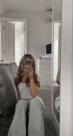 a woman sitting on the floor taking a selfie in front of a mirror with her cell phone