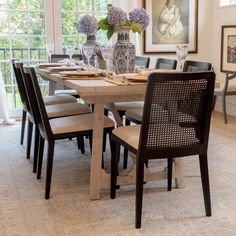 a dining room table with chairs and vases on it's centerpiece in front of a window