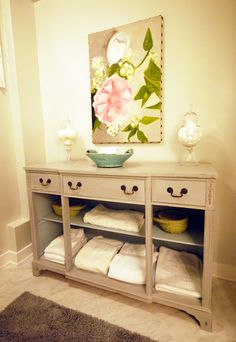 a white dresser with towels on it and a painting hanging above the drawers in front of it