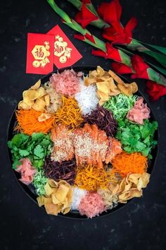 a black plate topped with lots of different types of food next to red and yellow flowers