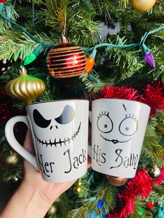 two coffee mugs with faces on them sitting in front of a christmas tree