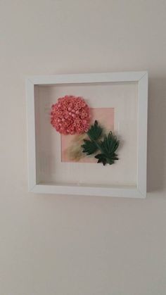 a white frame holding a pink flower and green leaf in it's center on the wall