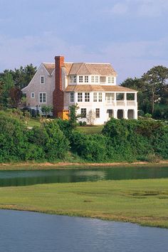 a large white house sitting on top of a lush green hillside next to a lake