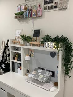 a white desk topped with a laptop computer next to a shelf filled with books and plants