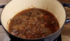 a blue pot filled with meat and sauce on top of a gas burner next to a wooden table