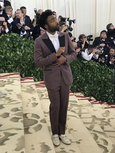 a man in a tuxedo and bow tie standing on a carpet with cameras around him