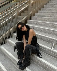 a woman sitting on some stairs with her legs crossed and wearing black boots, sunglasses and knee pads