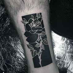 a black and white rose tattoo on the left inner arm, with leaves around it