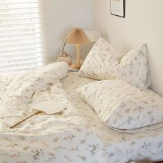 an unmade bed in a bedroom next to a lamp and window with shutters