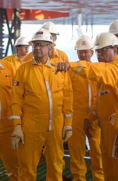 several men in yellow work suits and hard hats are pointing at something while standing next to each other