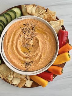 a bowl of hummus surrounded by vegetables and crackers on a wooden platter