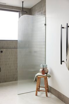 a bathroom with a stand up shower next to a stool and towel rack on the wall