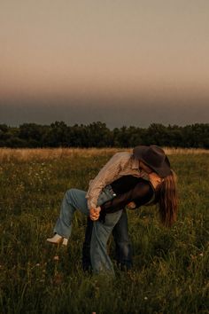 a man and woman are kissing in a field at sunset with the sun setting behind them