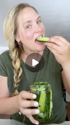 a woman holding a pickle in her mouth while eating something out of a jar