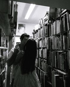 two people standing in front of a bookshelf with lots of books on the shelves