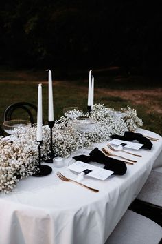 the table is set with white flowers and black napkins on it, along with candles