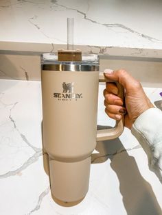 a person holding a coffee cup on top of a marble countertop next to a purple flower