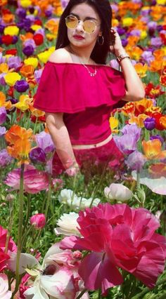 a woman wearing glasses standing in a field of flowers