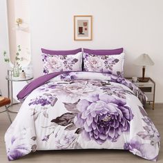 a bed with purple flowers on it in a room next to a table and chair