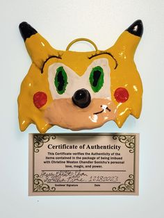 a yellow and black mask with green eyes on top of a plaque that says certificate of authenticity