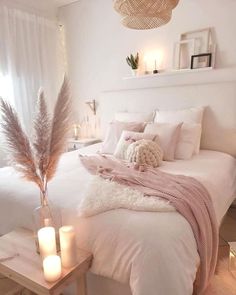 a white bed with pillows and blankets on top of it next to two lit candles