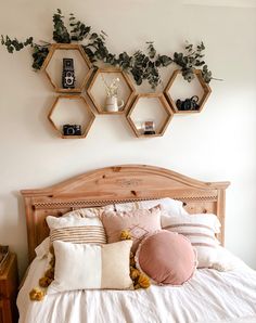 a bed with white sheets, pillows and plants on the wall above it is surrounded by hexagonal shelves