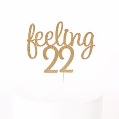 a cake topper with the words feeling 22 on it in gold sparkles against a white background