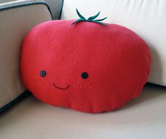 a red pillow sitting on top of a white couch next to a pillow with a smiling face