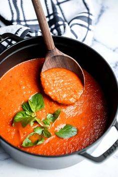 a pot filled with red sauce and garnished with green leaves on the spoon